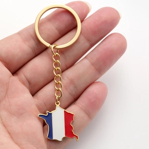 Détail d'un porte-clés carte de France en acier doré avec émail tricolore tenu à la main
