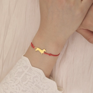 Detail of red braided cord bracelet featuring a gold dachshund dog charm on model wrist
