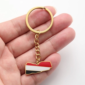 Close-up of golden Yemen map keychain with enamel flag colors held in hand