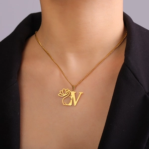 Gros plan détaillé du pendentif doré lettre N avec fleur de lotus et visage sur modèle
