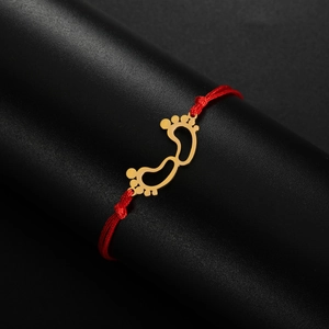 Detailed macro view of gold baby footprints charm on a red handmade woven bracelet