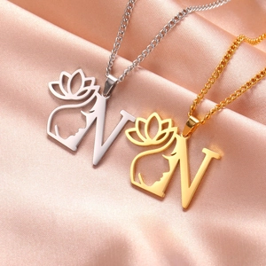 Détail des colliers lettre N en or et argent avec lotus sur fond de soie rose élégant