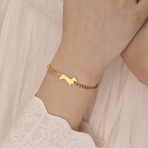 Polished gold dachshund pendant on box chain bracelet worn on a woman's wrist