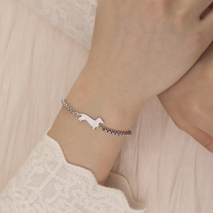 Close-up of a silver dachshund dog pendant on a box chain bracelet worn on a wrist