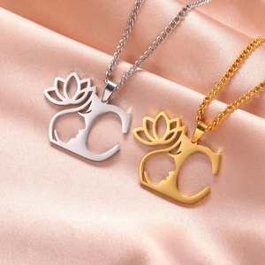 Gros plan de colliers en or et argent avec lotus et lettre sur fond de soie rose élégant
