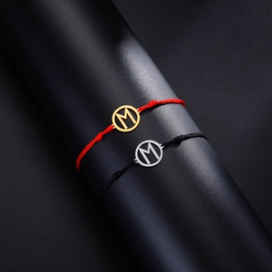Detailansicht von geflochtenen Armbändern mit Gold- und Silberanhängern Buchstabe M