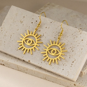Golden sun evil eye drop earrings on beige travertine stone display for a premium aesthetic