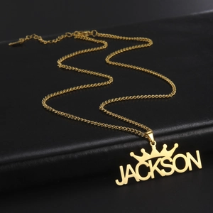 Detailed close-up of golden custom name necklace with crown icon on black leather background