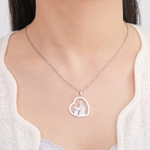 Detail des Herzanhängers mit Mutter-Kind-Silhouette auf weißem Spitzenkleid