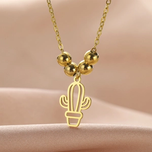 Macro shot of gold hollow cactus pendant with metal beads on elegant satin fabric
