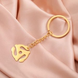 Detailed shot of golden 45 RPM record adapter keychain on elegant pink silk background