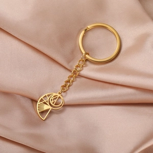 Detail of a golden stainless steel keychain with a hollow conch pendant on silk fabric