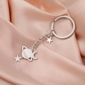 Detailed view of silver stainless steel Saturn and star charms on a silk background