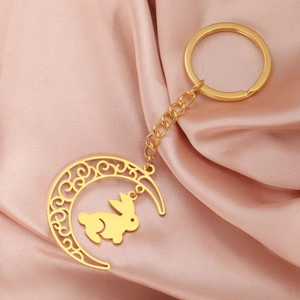 Détail du porte-clés doré lune et lapin sur un tissu en soie de couleur champagne