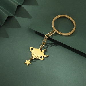 Detail of golden stainless steel Saturn and crescent moon keychain on green textured paper
