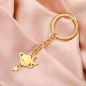 Detailed close-up of a golden Saturn planet keychain with moon and star charms on pink satin