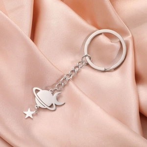 Detail of silver planet moon and star charms on stainless steel keychain with satin background