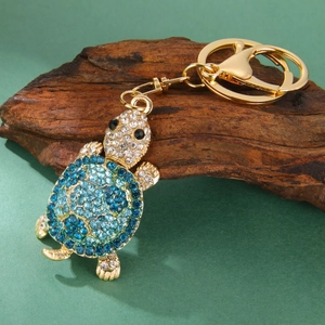 Detailed view of turtle keychain with blue rhinestones on a rustic wooden stand