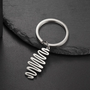 Polished silver stainless steel spiral wavy pendant keychain on a black rock surface