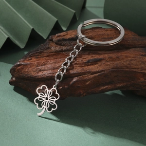 Polished stainless steel four-leaf clover keychain with heart cutouts on dark wood background