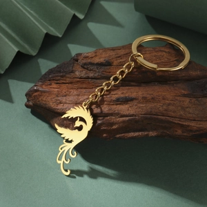 Polished gold phoenix pendant keychain made of durable stainless steel on a rustic wood base