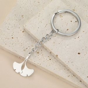 Polished stainless steel ginkgo leaf keychain on minimalist beige travertine stone stand