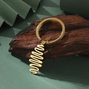 Polished gold stainless steel keychain with minimalist spiral pendant on a wood display
