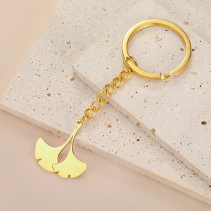 Close-up of golden ginkgo leaf pendant keychain on minimalist beige travertine stone