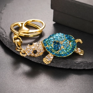 Detail shot of turtle keychain with blue rhinestones on a textured black stone surface