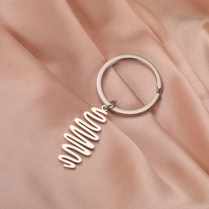 Close-up of minimalist stainless steel wave pendant keychain on pink silk fabric