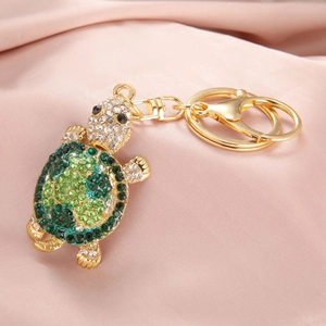 Detailed side view of golden turtle keychain with green rhinestones on pink silk background