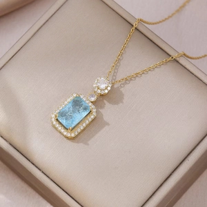 Elegante gouden ketting met een rechthoekige blauwe kristallen hanger op een fluwelen doos