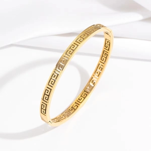 Vintage golden stainless steel bangle with Greek meander cutout on white satin cloth