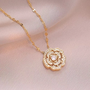 Elegant gold camellia flower pendant necklace with white zircon pavé on satin background