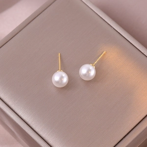 Nahaufnahme eleganter creme-weißer Perlenohrringe auf einer goldenen Box