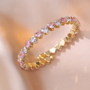 Makroansicht des goldenen Tennisarmbands mit rosa und weißen Zirkonia-Herzen in Fassung