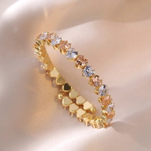 Nahaufnahme des goldenen Armbands mit herzförmigen Zirkonia auf Champagner-Stoff