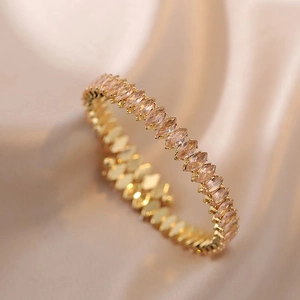 Eleganter Goldarmreif mit champagnerrosa Zirkonia im Marquiseschliff auf Seidenhintergrund