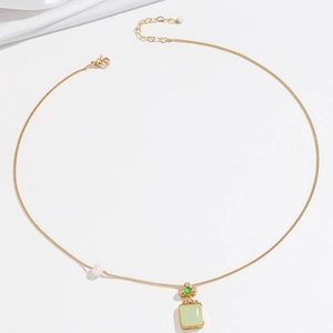 Dettaglio di una collana in oro con gemma verde e perla bianca su tessuto di seta