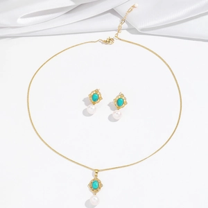 Parure de bijoux dorés avec pierres turquoises et perles blanches sur fond de soie