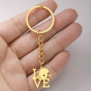 Detailansicht eines goldenen LOVE-Schlüsselanhängers mit Rugby-Helm-Anhänger in der Hand