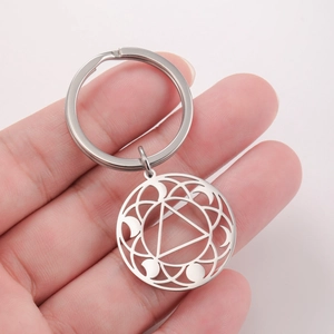 Stainless steel geometric keychain with hollow chakra symbol held against a pink background