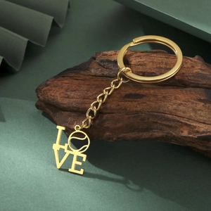 Detailansicht eines goldfarbenen LOVE-Schlüsselanhängers mit Tennisball-O auf dunklem Holz