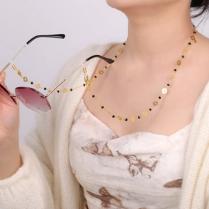 Détail d'une chaîne à lunettes dorée avec perles noires et étoiles sur un mannequin