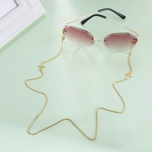 Détail de la chaîne de lunettes dorée avec petits pendentifs avion sur un fond vert pastel