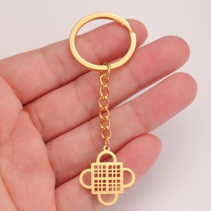 Golden Adinkra symbol keychain in polished stainless steel held in hand over pink background