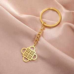 Detailed shot of golden Adinkra symbol keychain on pink silk background with keyring