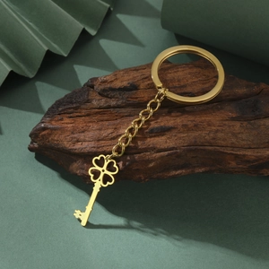 Detailed view of a golden stainless steel four-leaf clover key pendant on dark wood