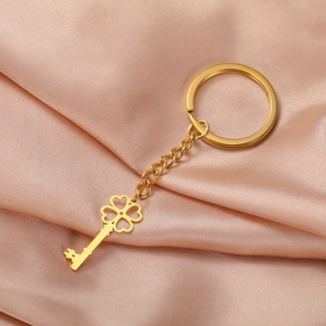 Close-up of golden four-leaf clover key pendant on smooth pink silk fabric