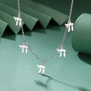 Detail van een zilveren ketting met vijf Hebreeuwse Chai-symbolen op een groene achtergrond